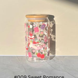 May include: A clear glass can-shaped tumbler with a bamboo lid, decorated with romantic-themed stickers. The stickers include hearts, roses, books, and glasses. The text "#009 Sweet Romance" is printed at the bottom.