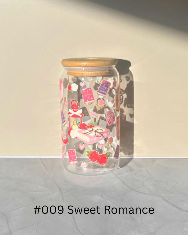 May include: A clear glass can-shaped tumbler with a bamboo lid, decorated with romantic-themed stickers. The stickers include hearts, roses, books, and glasses. The text "#009 Sweet Romance" is printed at the bottom.