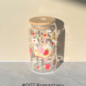 May include: Clear glass can-shaped tumbler with a bamboo lid. The glass is decorated with romantic-themed illustrations, including roses, hearts, and books. The text "#007 Romantasy" is printed at the bottom.