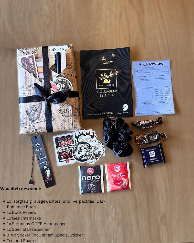 May include: A gift box with a wrapped book, face mask, scrunchie, bookmark, stickers, tea, and snacks. The book is wrapped in paper with a black ribbon. The face mask is black with white text. The bookmark has text.