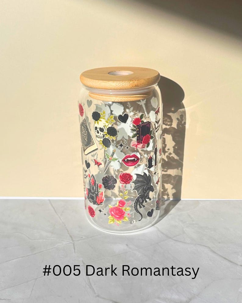 May include: A clear glass tumbler with a bamboo lid, decorated with gothic-themed stickers. The stickers include a skull, roses, a dragon, and a book. The text "#005 Dark Romantasy" is printed at the bottom of the glass.