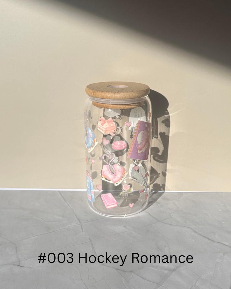 May include: A clear glass can-shaped tumbler with a wooden lid, decorated with pastel-colored illustrations of gifts, purses, and hearts. The text "#003 Hockey Romance" is printed at the bottom.