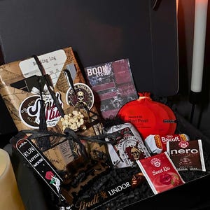 May include: A black gift box filled with various items. Includes a reading log, a book review, a red pomegranate-shaped item, a Lindt chocolate bar, and other small packages. The box is decorated with gothic-themed elements.
