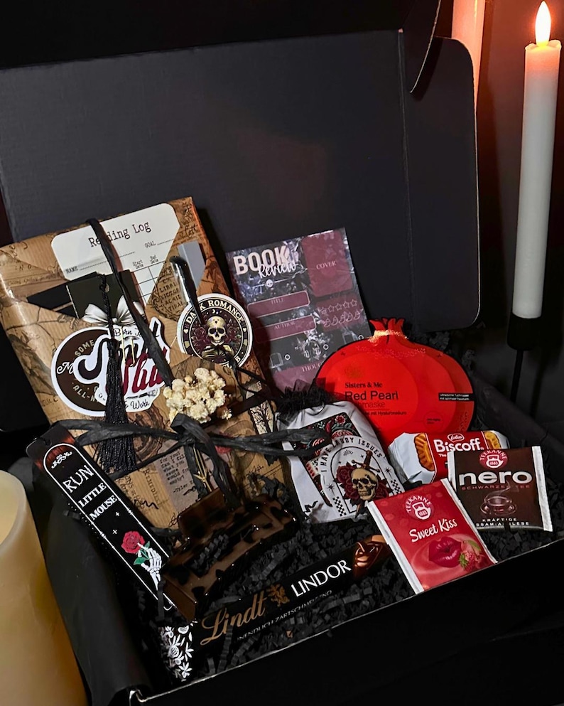 May include: A black gift box filled with various items. Includes a reading log, a book review, a red pomegranate-shaped item, a Lindt chocolate bar, and other small packages. The box is decorated with gothic-themed elements.