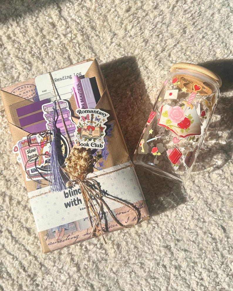 Könnte beinhalten: Ein Geschenkset für Bücherliebhaber, bestehend aus einem verpackten Paket mit Aufklebern, einer Quaste und Trockenblumen, sowie einem Glas mit Holzdeckel. Das Paket enthält den Text "Reading Log" und "Romantasy Book Club".