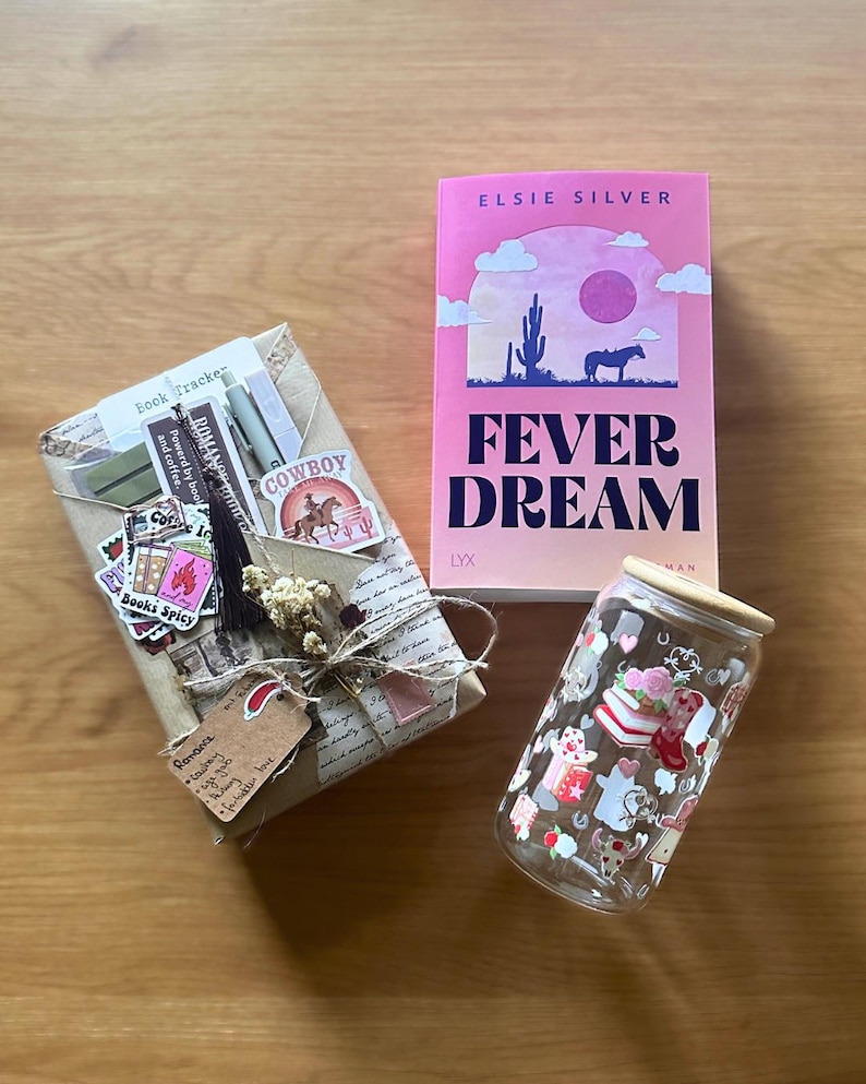 May include: An image featuring a wrapped gift, a pink book titled "Fever Dream", and a glass can with a wooden lid. The book cover displays a desert scene with a horse. The gift is adorned with stickers and a tag.
