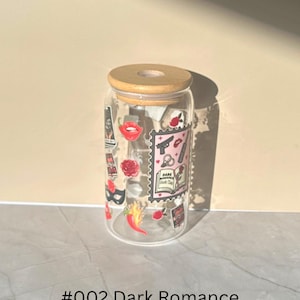 May include: A clear glass tumbler with a wooden lid, adorned with stickers featuring a red lip, a rose, a gun, and the text "Dark Romance Book Club." The tumbler is labeled "#002 Dark Romance."