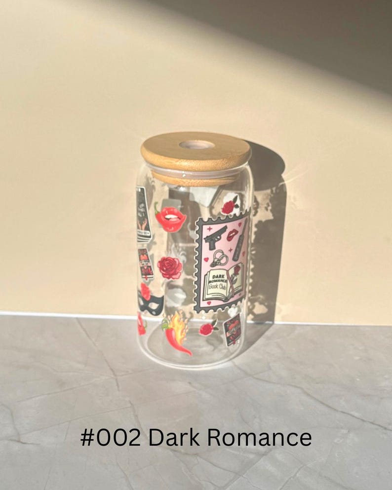 May include: A clear glass tumbler with a wooden lid, adorned with stickers featuring a red lip, a rose, a gun, and the text "Dark Romance Book Club." The tumbler is labeled "#002 Dark Romance."