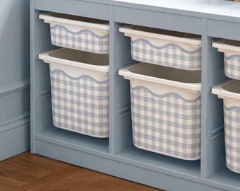 Puede incluir: Una unidad de almacenamiento de madera azul claro con tres compartimentos abiertos que contienen cajas de plástico blancas. Cada caja presenta un patrón de cuadros vichy azul claro y blanco con un borde superior festoneado. Libros sobre la superficie.