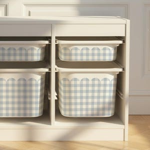 Puede incluir: Un mueble de almacenamiento blanco con seis compartimentos, cada uno con un contenedor extraíble. Los contenedores tienen un patrón de cuadros vichy azul claro y blanco. El mueble está contra una pared blanca y un suelo de madera.