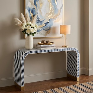 Mesa de console com detalhes em osso listrado azul e base curva dourada para hall de entrada.
