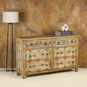 May include: A hand-painted wooden dresser with six drawers and a floral pattern in shades of green, red, and yellow. The dresser has black hardware and a light yellow top. A white vase and books are on top.