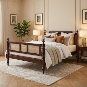 Könnte beinhalten: Ein dunkler Holzrahmen mit einem Kopf- und Fußteil aus geflochtenem Rohr. Das Bett ist mit weißer Bettwäsche, Kissen und einer beigefarbenen Decke bezogen. Der Raum hat eine neutrale Farbpalette mit gerahmten Kunstwerken und einem gemusterten Teppich.