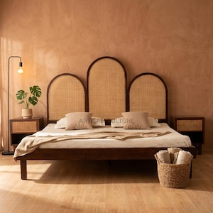 Puede incluir: Una cama de madera con cabecero tejido y mesitas de noche a juego. El cabecero tiene tres secciones arqueadas con un diseño de mimbre tejido. La cama está hecha con almohadas y una manta. Una cesta tejida con mantas enrolladas se encuentra al pie de la cama.