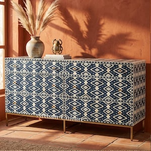 Puede incluir: Cómoda de seis cajones con un patrón geométrico azul marino y crema. La cómoda tiene herrajes y patas doradas. Un jarrón con plantas secas y objetos decorativos se encuentra encima. La cómoda mide aproximadamente 150 cm de ancho.
