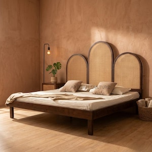 Könnte beinhalten: Ein dunkler Holzrahmen mit einem Kopfteil aus geflochtenem Rattan. Das Kopfteil hat drei bogenförmige Abschnitte. Das Bett hat eine hellfarbige Matratze mit Kissen und einer Decke. Der Text "ARTISAN CULTURE" ist auf den Kissen zu sehen.