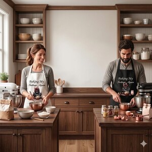May include: Two people wearing aprons that say "Baking My Feelings Again" are in a kitchen. The aprons have a graphic of a cat. They are using copper bowls and a stand mixer. The kitchen has wooden cabinets and shelves.