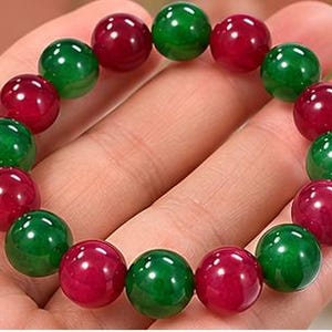 May include: A beaded bracelet featuring alternating smooth, spherical beads in deep emerald green and vibrant ruby red. The beads are polished to a high shine and are strung together in a circular pattern to form a continuous, flexible wrist accessory.