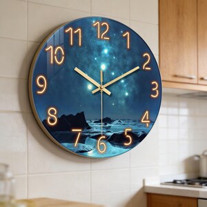 Peut inclure: Horloge murale ronde avec un cadre doré. Le cadran de l'horloge présente une scène de ciel nocturne avec un paysage en bas et des chiffres orange lumineux. Les aiguilles sont dorées.