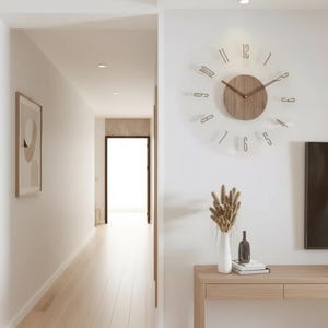 May include: A modern wooden wall clock with a light brown face and dark brown hands and numerals. The clock is mounted on a white wall. A wooden console table with a white vase, a dark bottle, and books is below the clock.