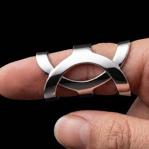 May include: A polished silver-toned metal finger splint featuring a curved, open-frame design with two intersecting arched bands that wrap around the finger. The structure is smooth, reflective, and rigid, providing a contoured fit for the digit.