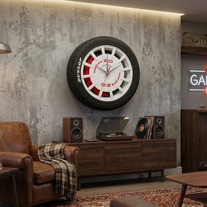 Puede incluir: Un gran reloj de pared con diseño de llanta. La esfera del reloj es blanca con detalles rojos y manecillas negras. El neumático tiene la palabra "Dunlop" en blanco. El reloj está montado en una pared de hormigón gris, con un sillón de cuero marrón y muebles de madera.