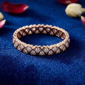 May include: Rose gold ring featuring a continuous pattern of heart-shaped settings, each encasing a small, sparkling diamond. The ring is set against a deep blue background, with hints of floral accents.