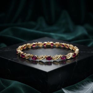 May include: A gold bracelet featuring a series of oval-cut deep red rubies alternating with small, clear, round-cut diamonds. The metal links between the stones have a polished finish, creating a continuous circular band of gemstones.