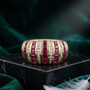 May include: A gold band ring featuring alternating vertical channels of square-cut red rubies and round brilliant-cut white diamonds. The design consists of four rows of rubies separated by three rows of diamonds, creating a wide, domed profile.