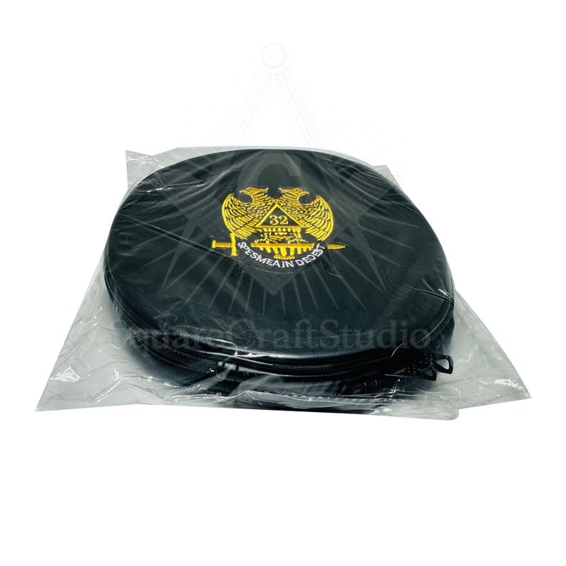 May include: Black round case with a gold emblem featuring a double-headed eagle, a number 32, and the text "SPES MEA IN DEO EST". The case is in a clear plastic bag. The case has a zipper closure.