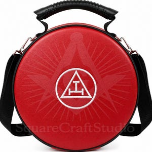 Op de afbeelding: Een ronde, rode tas met een zwarte handgreep en schouderriem. De tas heeft een wit embleem in een cirkel en een groter, vervaagd embleem op de achtergrond. De tekst "SquareCraftStudio" staat onderaan.