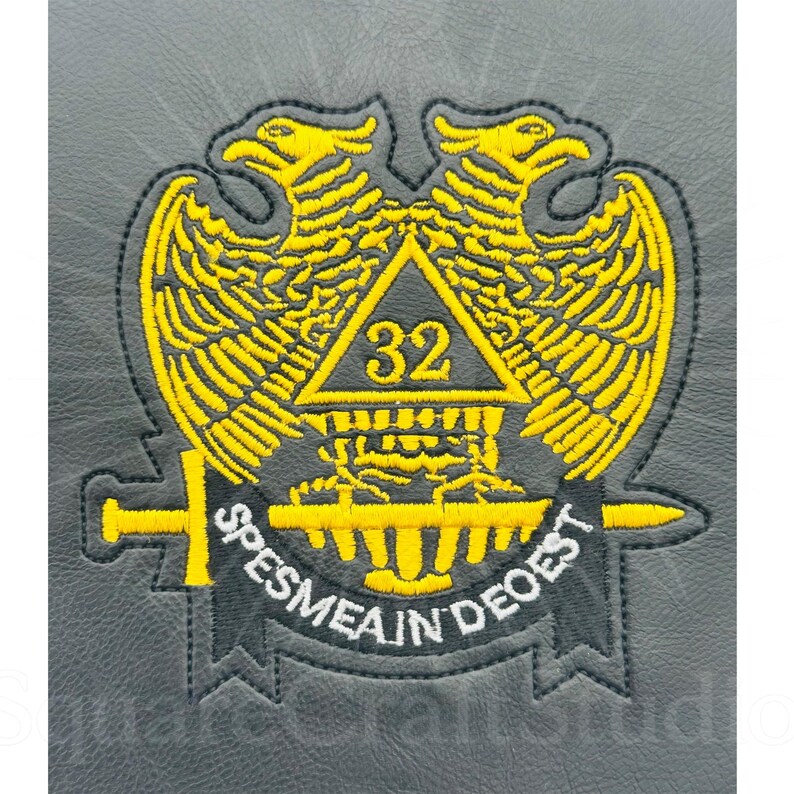 May include: Embroidered patch featuring a yellow double-headed eagle design with outstretched wings, a triangle with the number 32, and the Latin phrase "SPES MEA IN DEO EST" on a banner. The patch is on a gray background.