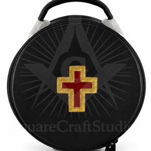May include: Black round case with a handle and silver accents. The case features a gold-bordered red cross emblem and a Masonic symbol design. The text "SquareCraftStudio" is visible on the bottom of the case.