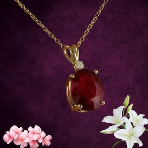 Könnte beinhalten: Eine goldene Halskette mit Anhänger, die einen großen, oval geschliffenen Rubin-Edelstein zeigt. Der Rubin ist in einer goldenen Lünette mit einem kleinen Diamantakzent darüber gefasst. Die Halskette hat eine zarte Goldkette.