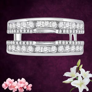 May include: A silver ring with two bands, each lined with multiple clear, round-cut gemstones. The ring has a modern, open design. The background is a deep purple with pink and white flowers.