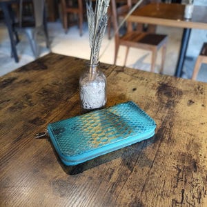 Op de afbeelding: Een witte keramische mok met een zwart handvat en de tekst "But First, Coffee" in een vetgedrukte, zwarte letter. De mok is gevuld met een donkere vloeistof, waarschijnlijk koffie, en staat op een lichtgekleurd oppervlak.