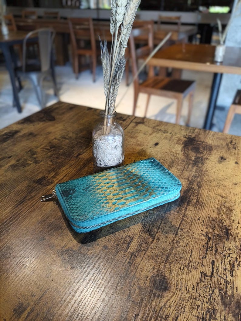 Op de afbeelding: Een witte keramische mok met een zwart handvat en de tekst "But First, Coffee" in een vetgedrukte, zwarte letter. De mok is gevuld met een donkere vloeistof, waarschijnlijk koffie, en staat op een lichtgekleurd oppervlak.