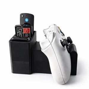 May include: A black charging station with a white game controller. The station has a slot for a remote with a microphone icon and a red and black control panel. The controller is white with black joysticks and coloured buttons.