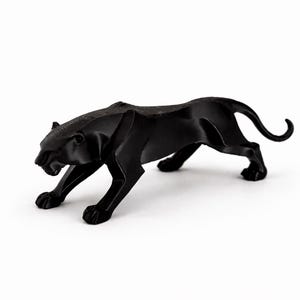 May include: A black panther ornament in a stalking pose. The sculpture is made of a solid, matte black material. The panther's body is sleek, with defined muscles and a curved tail. The ornament is set against a plain white background.