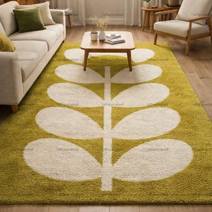 May include: A rectangular area rug featuring a deep olive green background with a large, centred, cream-coloured stylised leaf pattern. The rug has a thick, plush, tufted texture and covers a significant portion of the floor space in the room.
