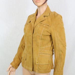 Peut inclure: Veste en daim moutarde avec une fermeture boutonnée, deux poches poitrine et deux poches inférieures. La veste présente des détails de couture blancs et un col cranté. Les manches sont longues, et la veste est présentée sur un mannequin.