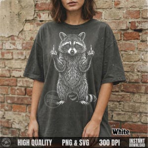 Woman standing by a brick wall wearing a dark grey t-shirt with a white hand-drawn style sassy raccoon graphic