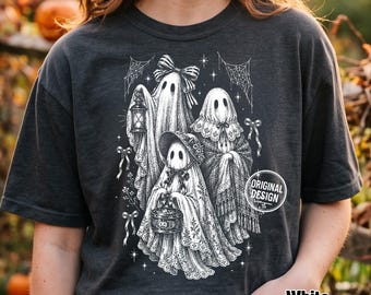 Może przedstawiać: Ciemnoszary t-shirt z białą grafiką przedstawiającą trzy duchy w koronkach, kokardach i czepkach. Jeden duch trzyma latarnię, drugi niesie małe wiaderko w kształcie dyni, a całość uzupełniają wzory pajęczyn oraz gwiazdek na ciemnym tle.