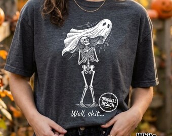 Może przedstawiać: Ciemnoszary t-shirt z krótkim rękawem z białą grafiką przedstawiającą szkielet w prześcieradle ducha na głowie. Pod szkieletem znajduje się napis "Well, shit..." oraz okrągła odznaka z napisem "ORIGINAL DESIGN".