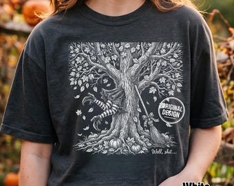 Może przedstawiać: Ciemnoszary t-shirt z białą grafiką przedstawiającą duże drzewo, z którego pnia wystaje para pasiastych nóg. Obok drzewa stoi miotła, a całość otaczają dynie i opadające liście. Napis na grafice brzmi, Well, shit...