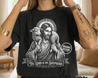 Może przedstawiać: Czarny t-shirt z białą grafiką przedstawiającą brodatą postać z aureolą trzymającą jagnię na ramionach. Poniżej postaci znajduje się baner z napisem The Lord is My Shepherd oraz Psalm 23 wykonanym białą czcionką.