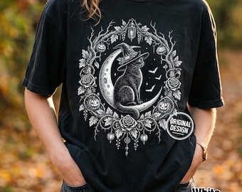 Może przedstawiać: Czarny t-shirt z białym nadrukiem graficznym przedstawiającym czarnego kota w kapeluszu czarownicy, siedzącego na półksiężycu. Wzór otoczony jest kolistym wieńcem z róż, liści i małych dyń, z dodatkiem latarni oraz latających nietoperzy.