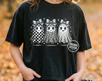 Może przedstawiać: Czarny t-shirt z krótkim rękawem z grafiką przedstawiającą trzy białe duszki w kokardkach. Duszki mają różne wzory: jeden w szachownicę, jeden w panterkę i jeden w kropki. Małe białe gwiazdki otaczają duszki, a okrągłe logo zawiera napis Original Design.