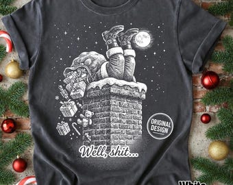 Może przedstawiać: Ciemnoszary t-shirt z białą grafiką przedstawiającą Świętego Mikołaja utkniętego do góry nogami w ceglanym kominie. Wzór zawiera spadające pudełka z prezentami, pluszowego misia, pełnię księżyca, gwiazdy oraz napis "Well, shit..." wydrukowany poniżej.