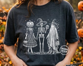 Może przedstawiać: Ciemnoszary t-shirt z białą grafiką przedstawiającą trzy postacie: osobę z głową dyni w sukience, szkielet w kapeluszu czarownicy trzymający czaszkę oraz ducha w kapeluszu czarownicy trzymającego torebkę na słodycze z napisem Trick or Treat.